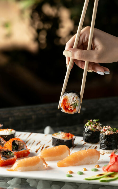 woman-holding-sushi-roll-with-chopsticks